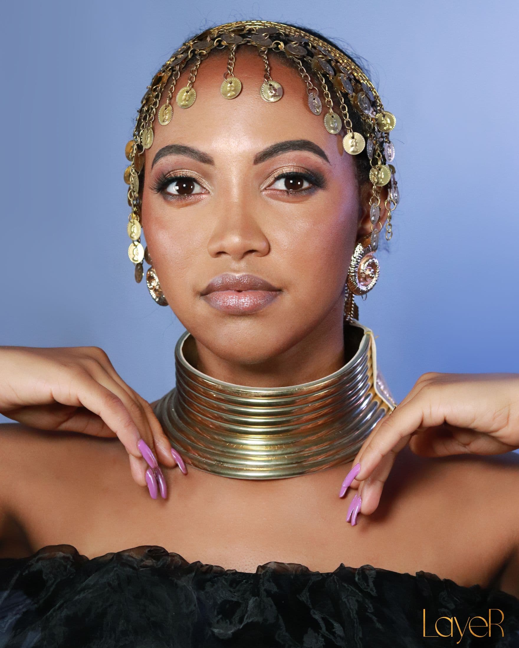 Beauty portrait with gold eyes, lilac nails and a coin headpiece against blue