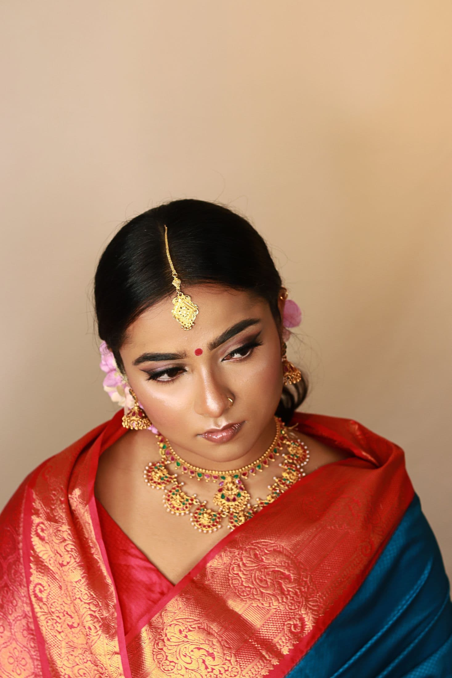 Bridal portrait with a red and blue silk saree, gold jewellery and soft rose makeup